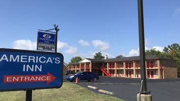 Señal de America's Inn con flecha indicando la entrada, estacionamiento y edificio de techo rojo y paredes de ladrillo.