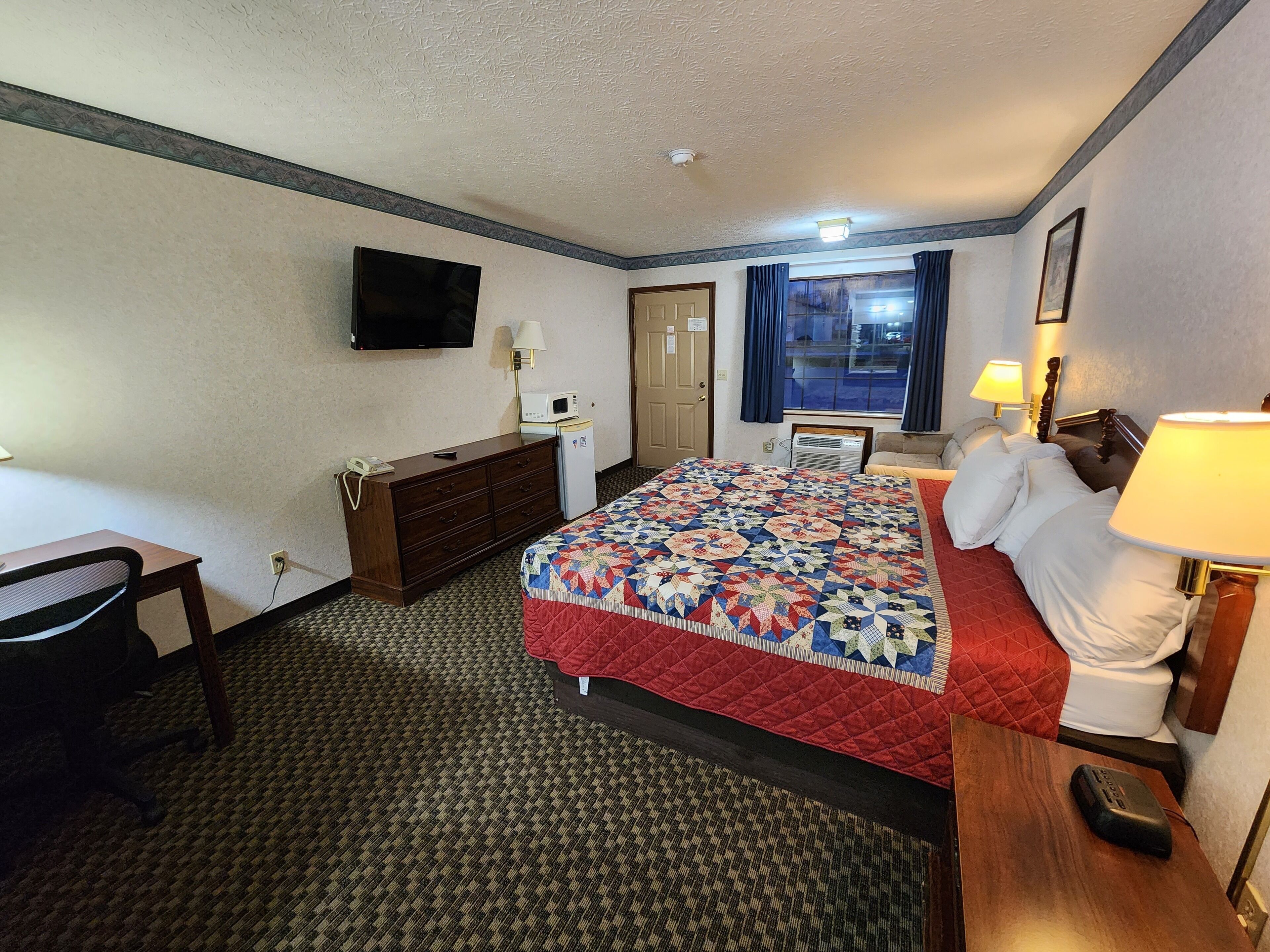 A hotel room with a bed, a desk, a dresser, a television, and a window with curtains.