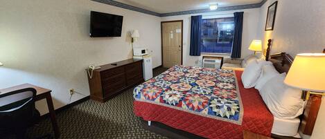 A hotel room with a bed, a desk, a dresser, a television, and a window with curtains.
