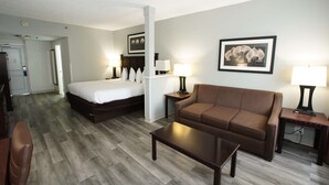 A hotel room with a bed, a brown sofa, a coffee table, and a desk with a lamp. - Best Western Paramus Hotel & Suites (Paramus)