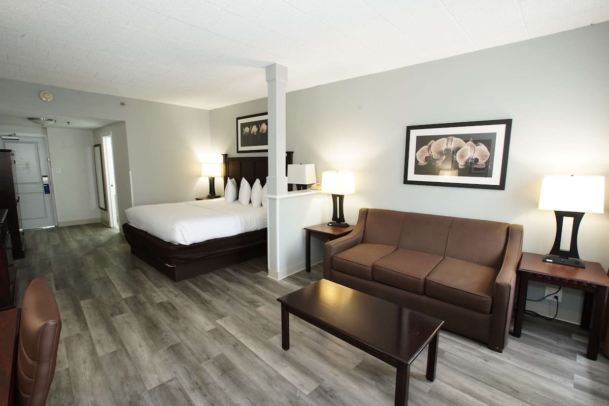 A hotel room with a bed, a brown sofa, a coffee table, and a desk with a lamp.