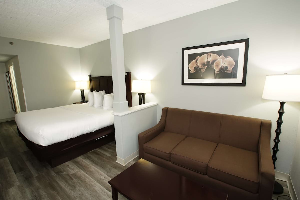 A hotel room with a bed, a brown sofa, a small table, a white pillar, and a framed picture on the wall.