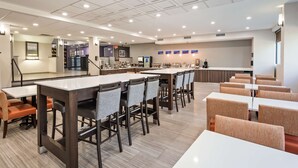 A modern dining area with multiple tables and chairs, a kitchen area with a coffee machine, and a counter with a menu display. - Best Western Paramus Hotel & Suites (Paramus)