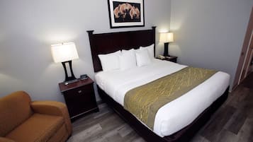 A hotel room with a large bed, two bedside tables with lamps, a brown armchair, and a framed picture on the wall.