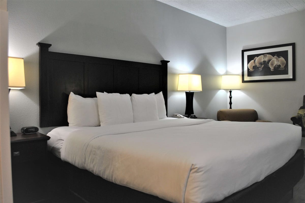 A hotel room with a large bed, two bedside tables, a nightstand, a wall-mounted lamp, and a framed picture.