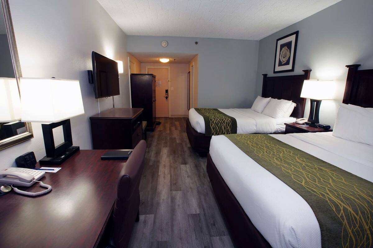 A hotel room with two beds, a desk with a telephone, a television, and a door leading to another room.