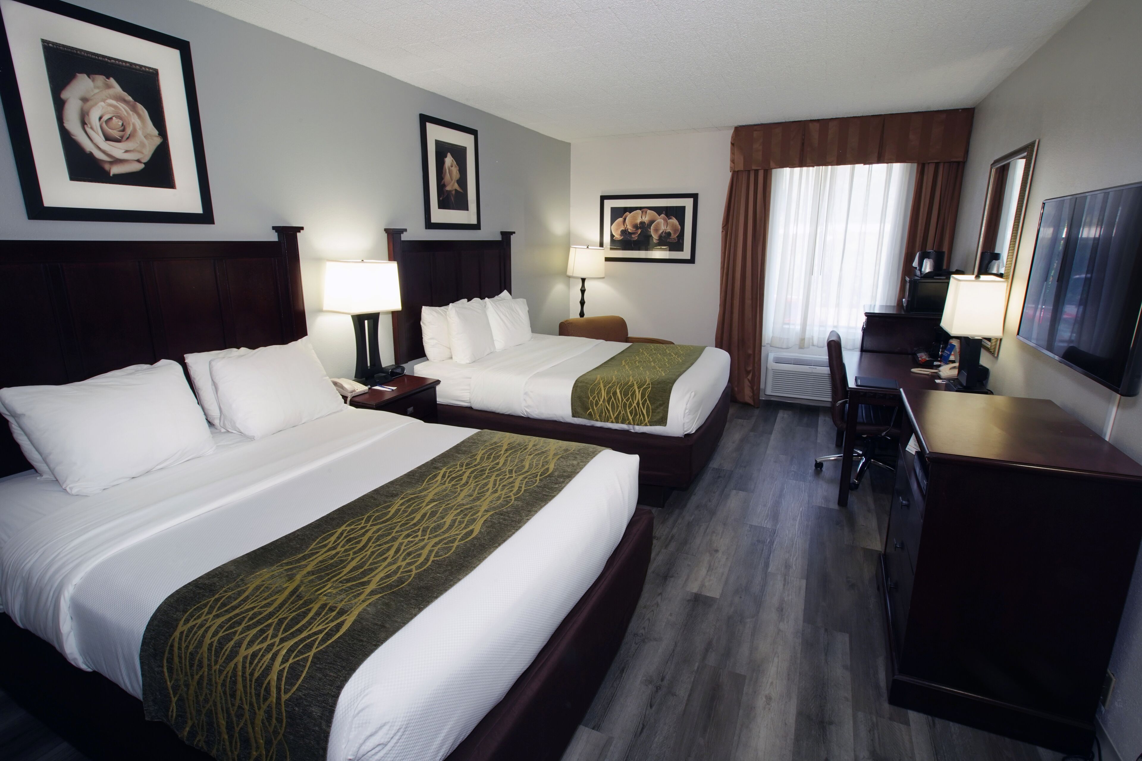 A hotel room with two beds, a desk, a chair, and a TV.