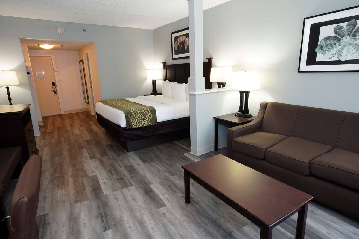 A hotel room with a bed, a sofa, a coffee table, and a desk with a lamp.