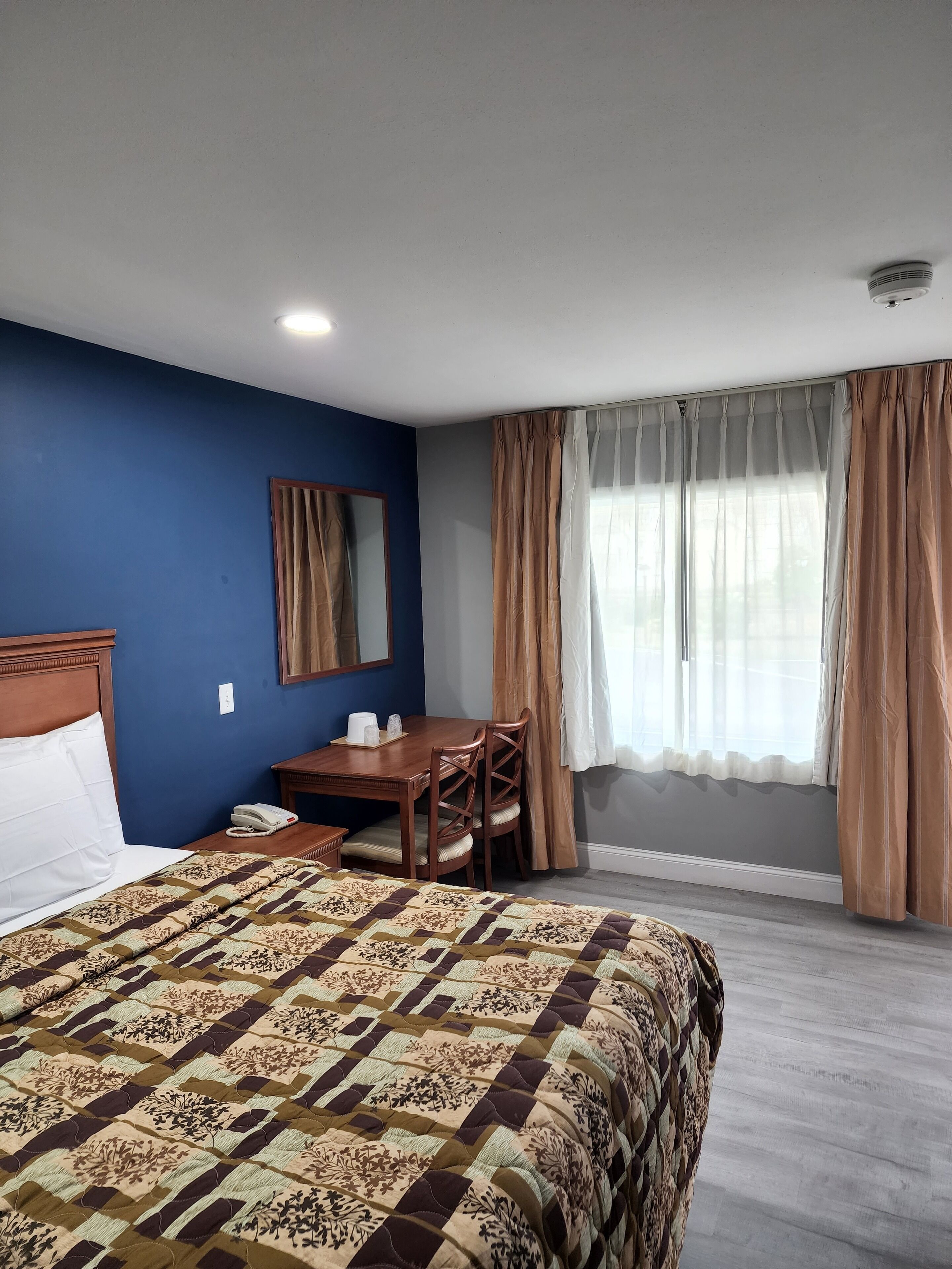 Una habitación de hotel con una cama, un escritorio, una silla, un espejo y una ventana con cortinas.