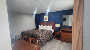 Una habitación de hotel con cama, escritorio, silla, cómoda, espejo y un cuadro en la pared.