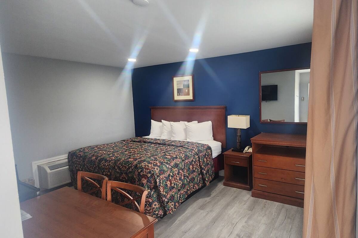 A hotel room with a bed, a desk, a chair, a dresser, a mirror, and a picture on the wall.