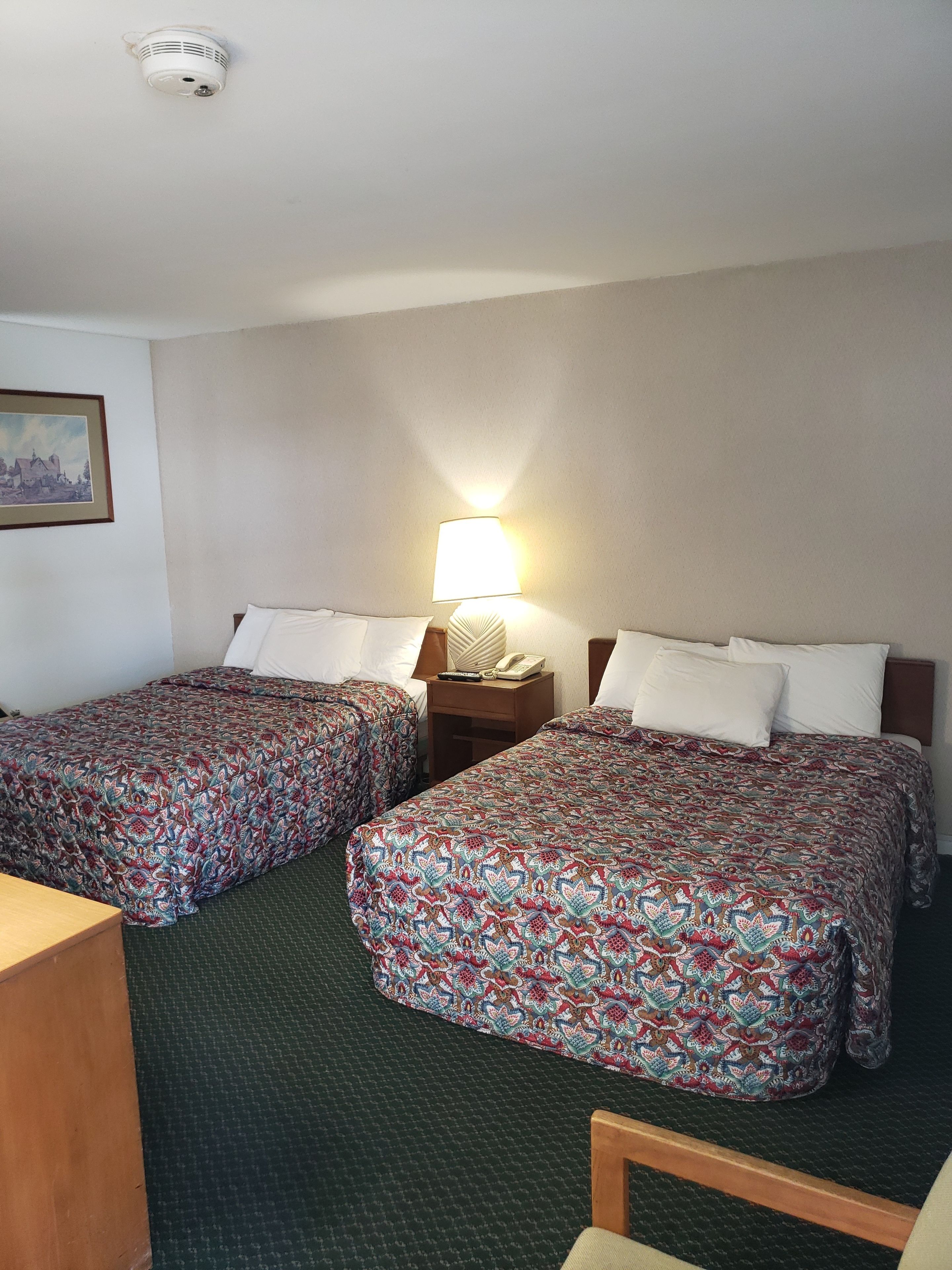 Ein Hotelzimmer mit zwei Betten, einem Nachttisch mit Lampe, einem Schreibtisch und einem Stuhl.