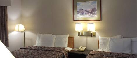 Una camera d'albergo con due letti, un comodino con una lampada, un quadro appeso alla parete e una scrivania della reception.