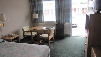 A hotel room with a bed, a desk with a chair, a television, a lamp, and a window with curtains.