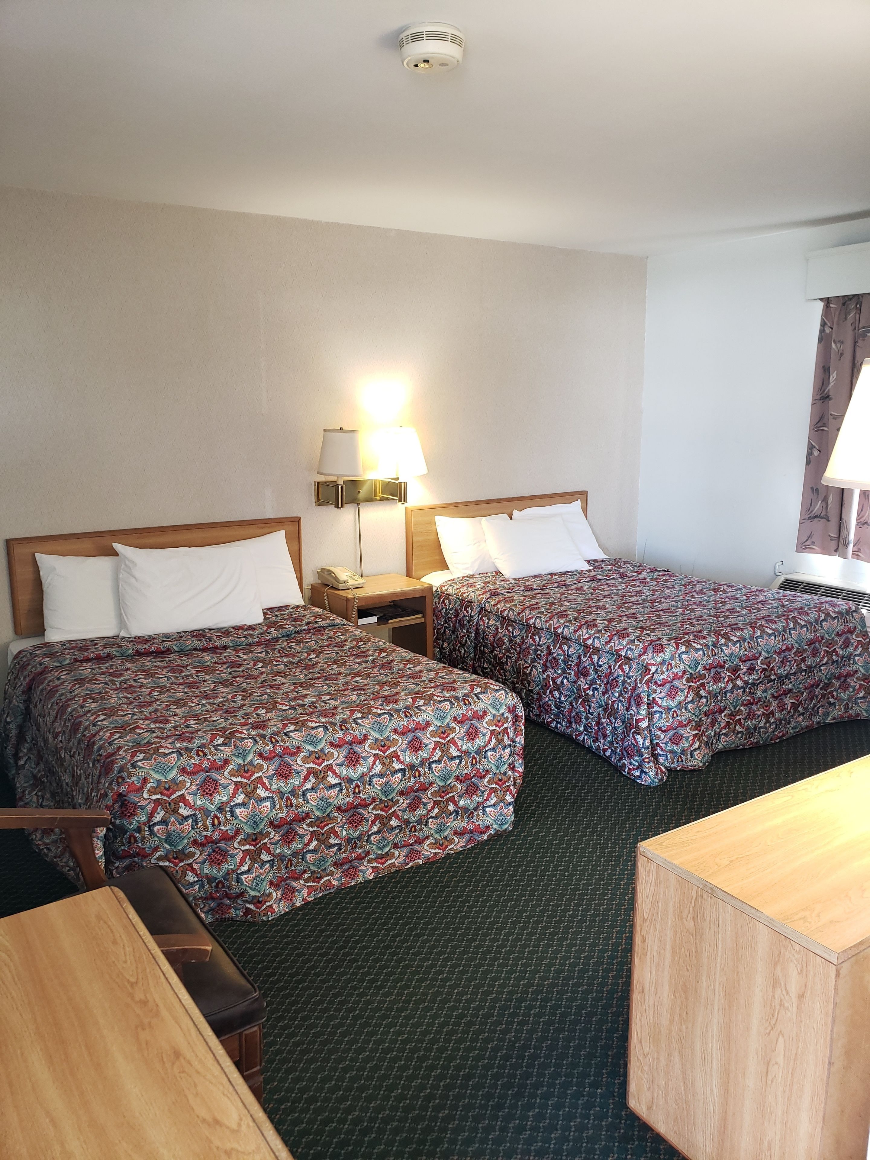 Une chambre d’hôtel avec deux lits, un bureau, une chaise, une lampe et un téléphone.