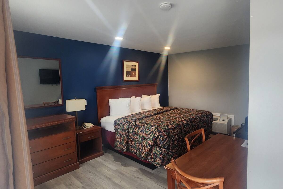 A hotel room with a bed, a desk, a chair, a dresser, a mirror, and a television.