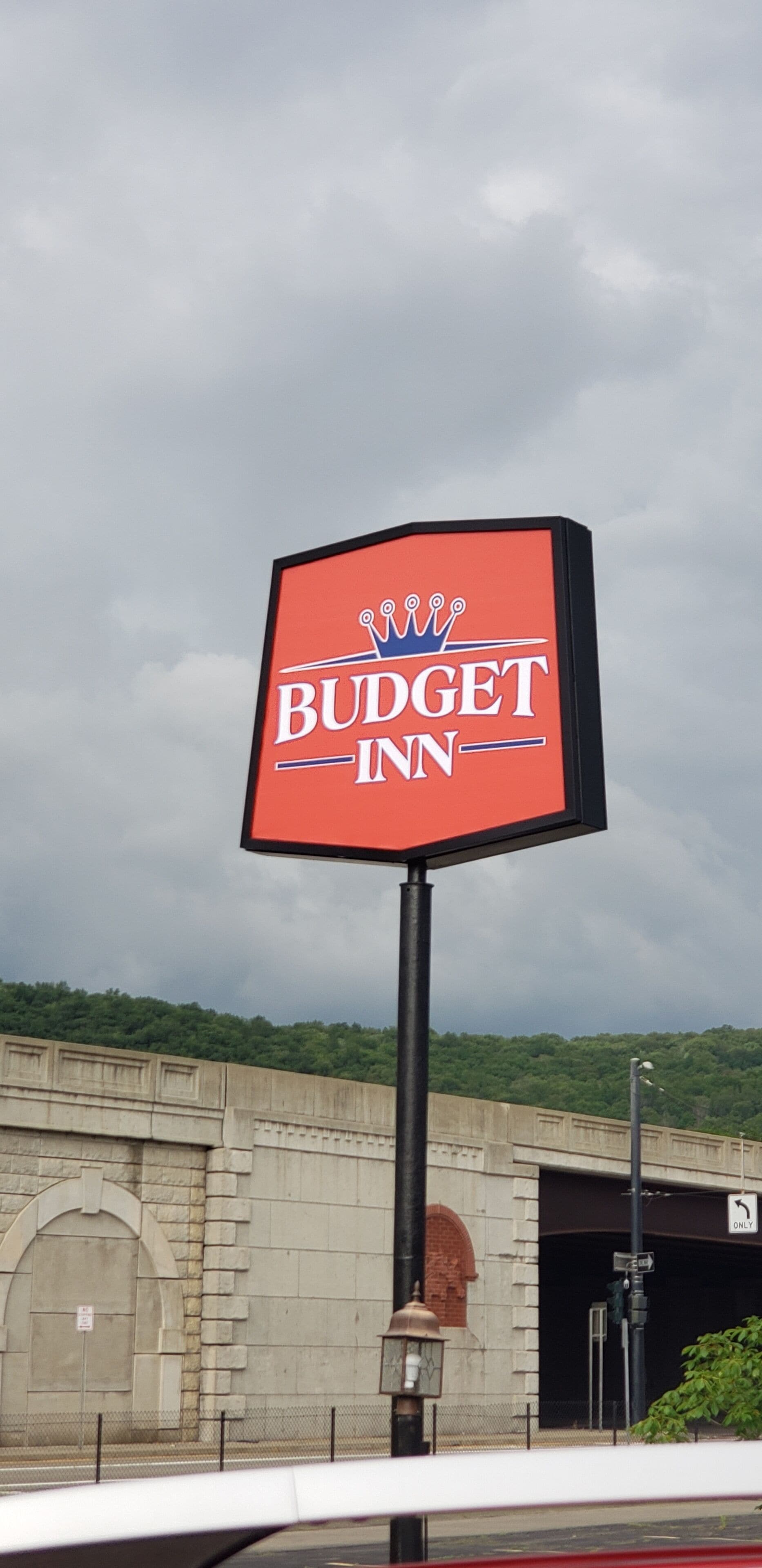 Segnaletica di Budget Inn con logo a forma di corona, su sfondo di cielo nuvoloso.