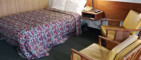 A hotel room with a bed, a chair, a bedside table with a lamp, and a framed picture on the wall.