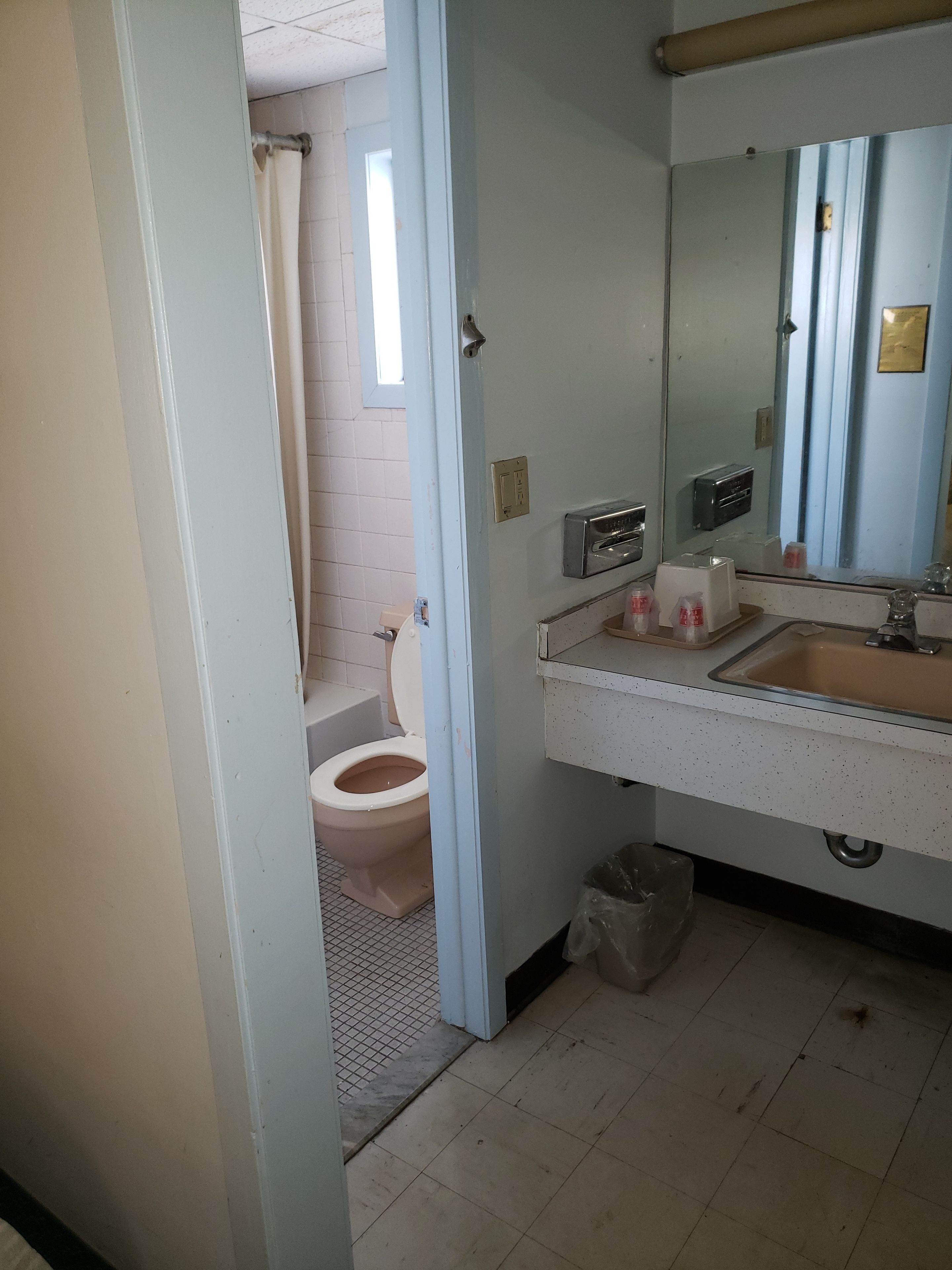 A bathroom with a toilet, sink, mirror, and a trash bin.
