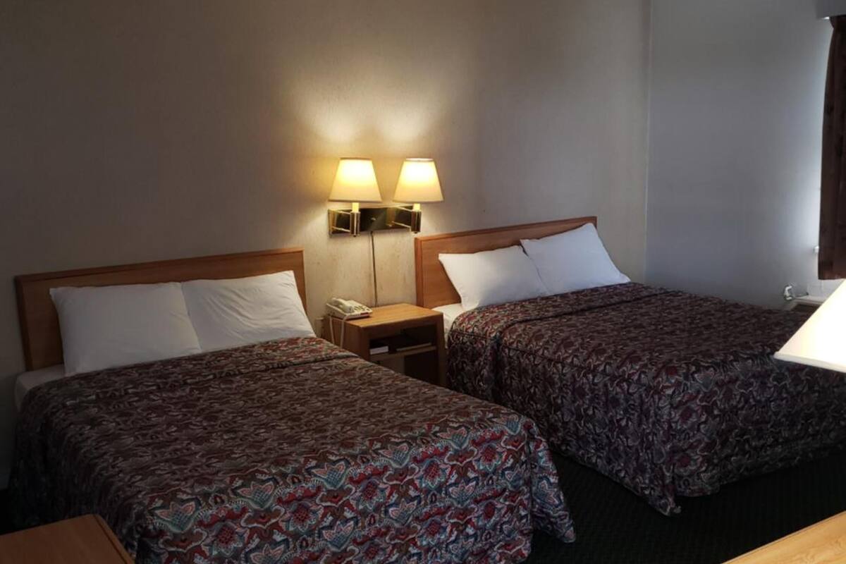A hotel room with two beds, a wooden nightstand, a desk, and two wall-mounted lamps.