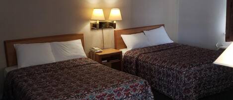 Una habitación de hotel con dos camas, una mesita de noche de madera, un escritorio y dos lámparas de pared.
