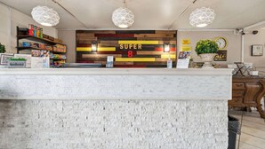 A reception area with a modern design, featuring a brick wall, a 'SUPER 8' sign, and a variety of products on shelves. - Super 8 by Wyndham Millbury/Toledo (Millbury)