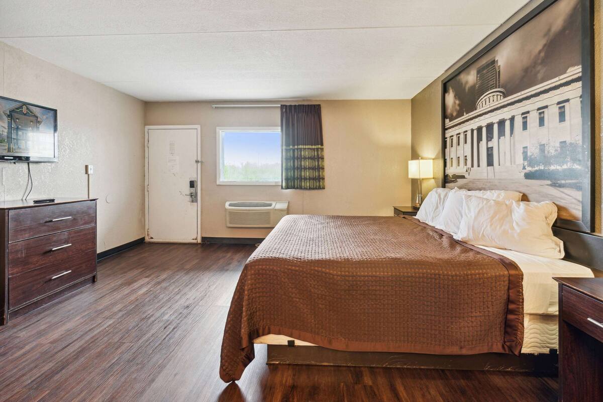 Een hotelkamer met een bed, een dressoir, een raam, een deur en een schilderij aan de muur.