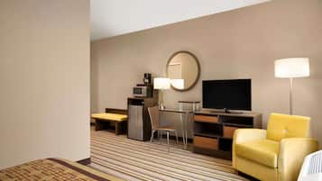 A hotel room with a bed, a desk with a chair, a television, a microwave, and a lamp.