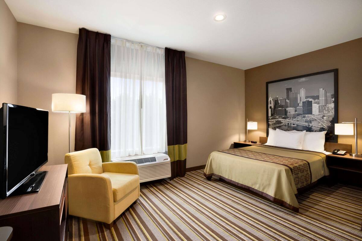 Habitación de hotel con cama, televisor, una silla y un cuadro de un paisaje urbano en la pared.