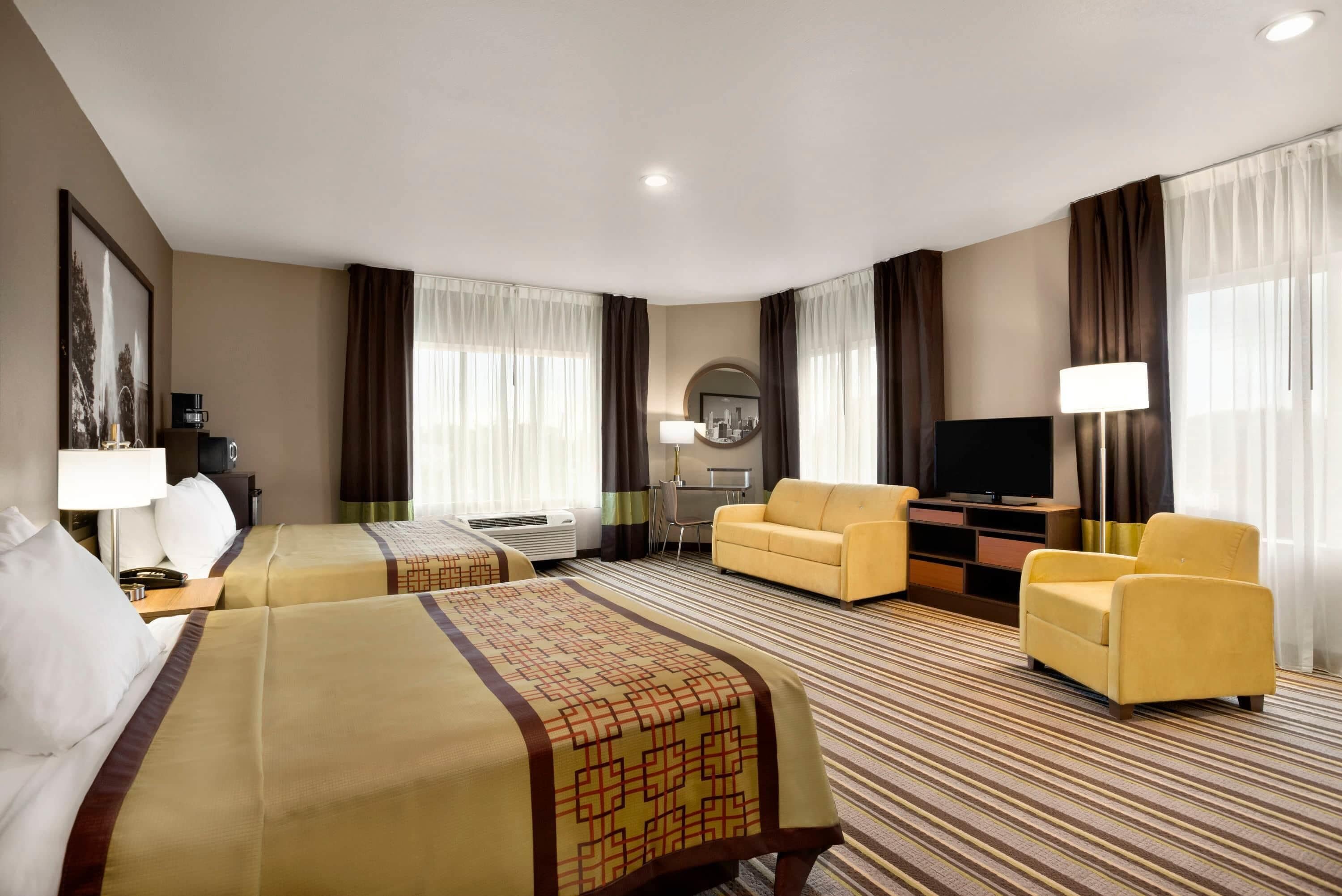 A hotel room with two beds, a sofa, a TV, and a desk with a lamp.