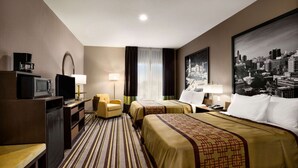 Ein Hotelzimmer mit zwei Betten, einem Schreibtisch, einem Fernseher, einem Kühlschrank, einem Sessel und einem Stadtbild an der Wand.