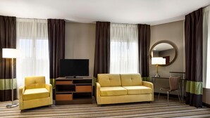 Ein Hotelzimmer mit Sofa, Sessel, Fernseher, Schreibtisch und Spiegel.