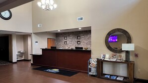 A hotel reception area with a wooden reception desk, a stone wall, a chandelier, a clock, and a fire alarm. - Days Inn & Suites by Wyndham Manheim Lebanon (Manheim)