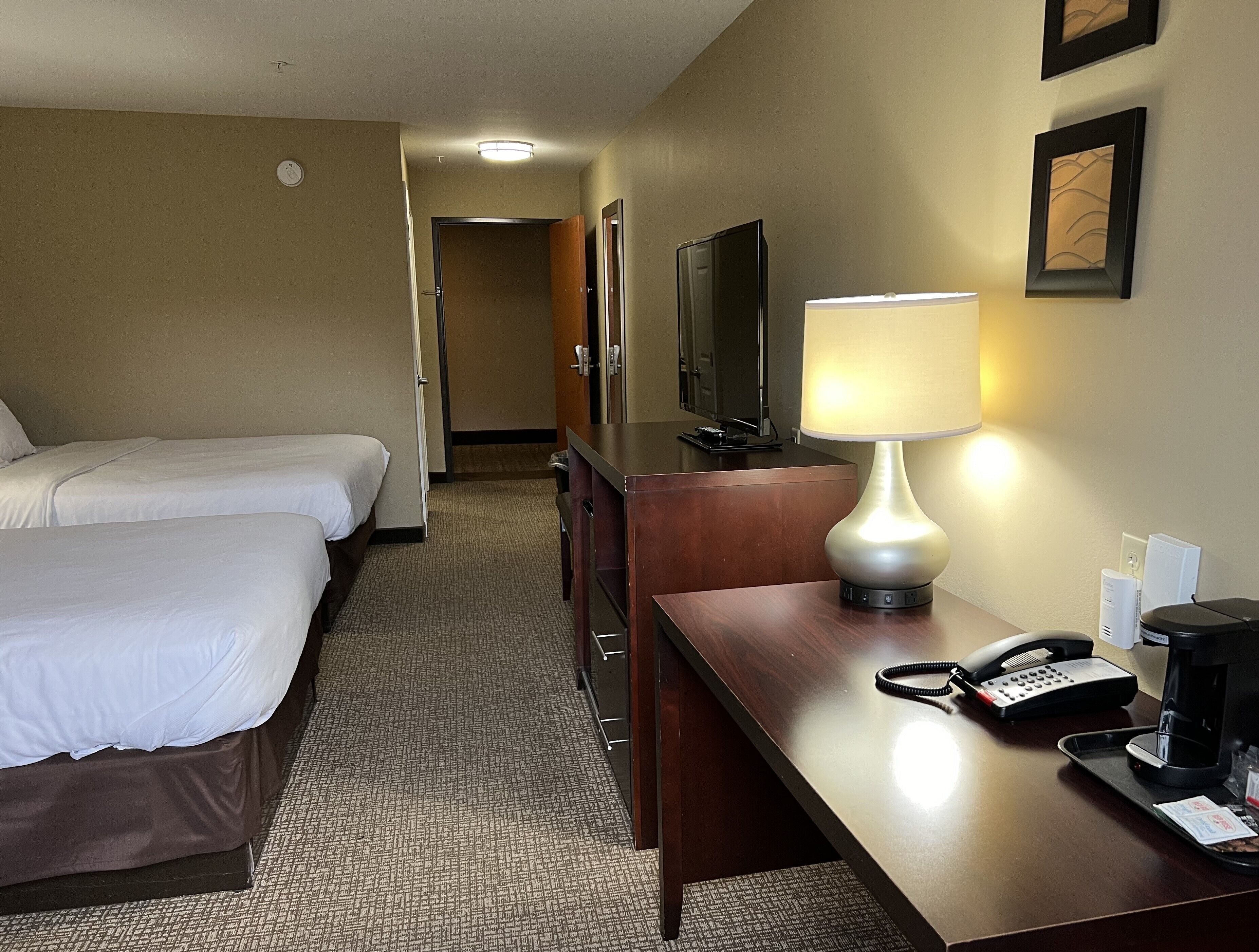 A hotel room with two beds, a desk with a lamp, a telephone, and a television.