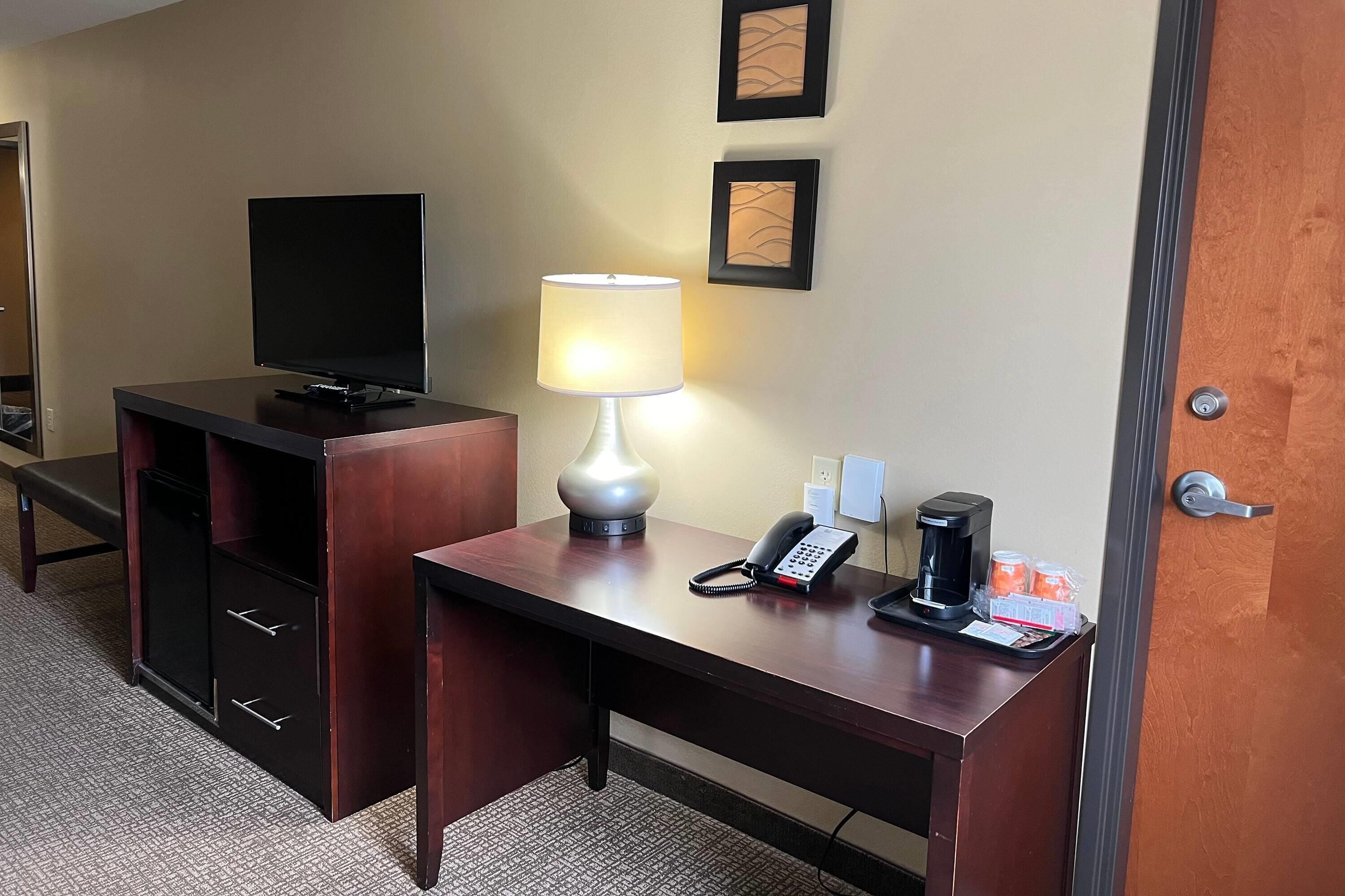 Una habitación de hotel con escritorio, televisión, lámpara, teléfono y cafetera.