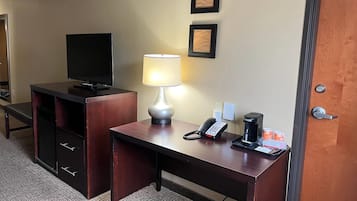 Una habitación de hotel con escritorio, televisión, lámpara, teléfono y cafetera.