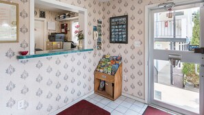 Un espace d’accueil avec un papier peint à motifs, un comptoir en bois, un présentoir à magazines et une porte donnant sur l’extérieur.