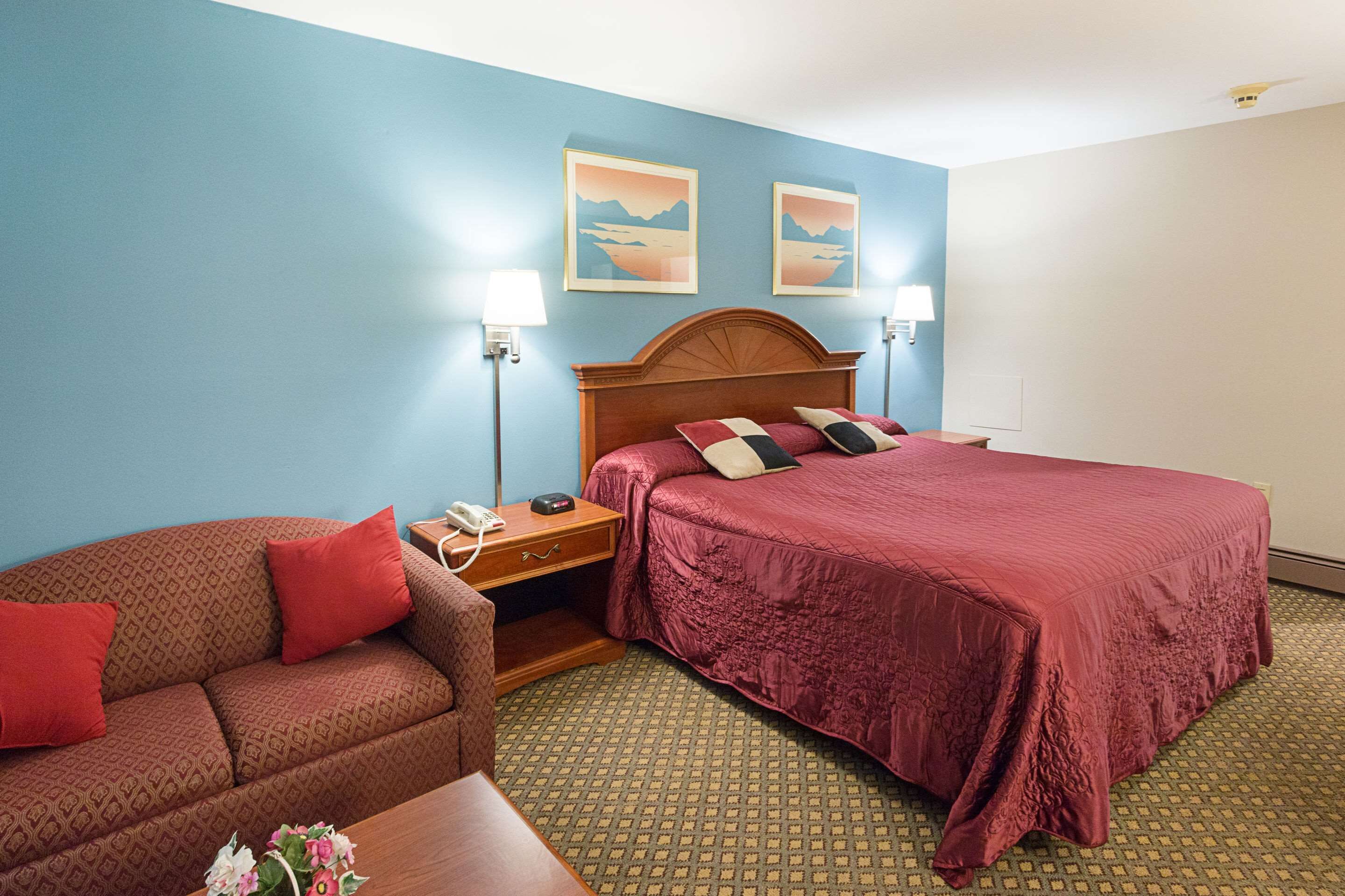 Une chambre d’hôtel comprenant un lit, un canapé, une table de chevet et deux lampes fixées au mur.