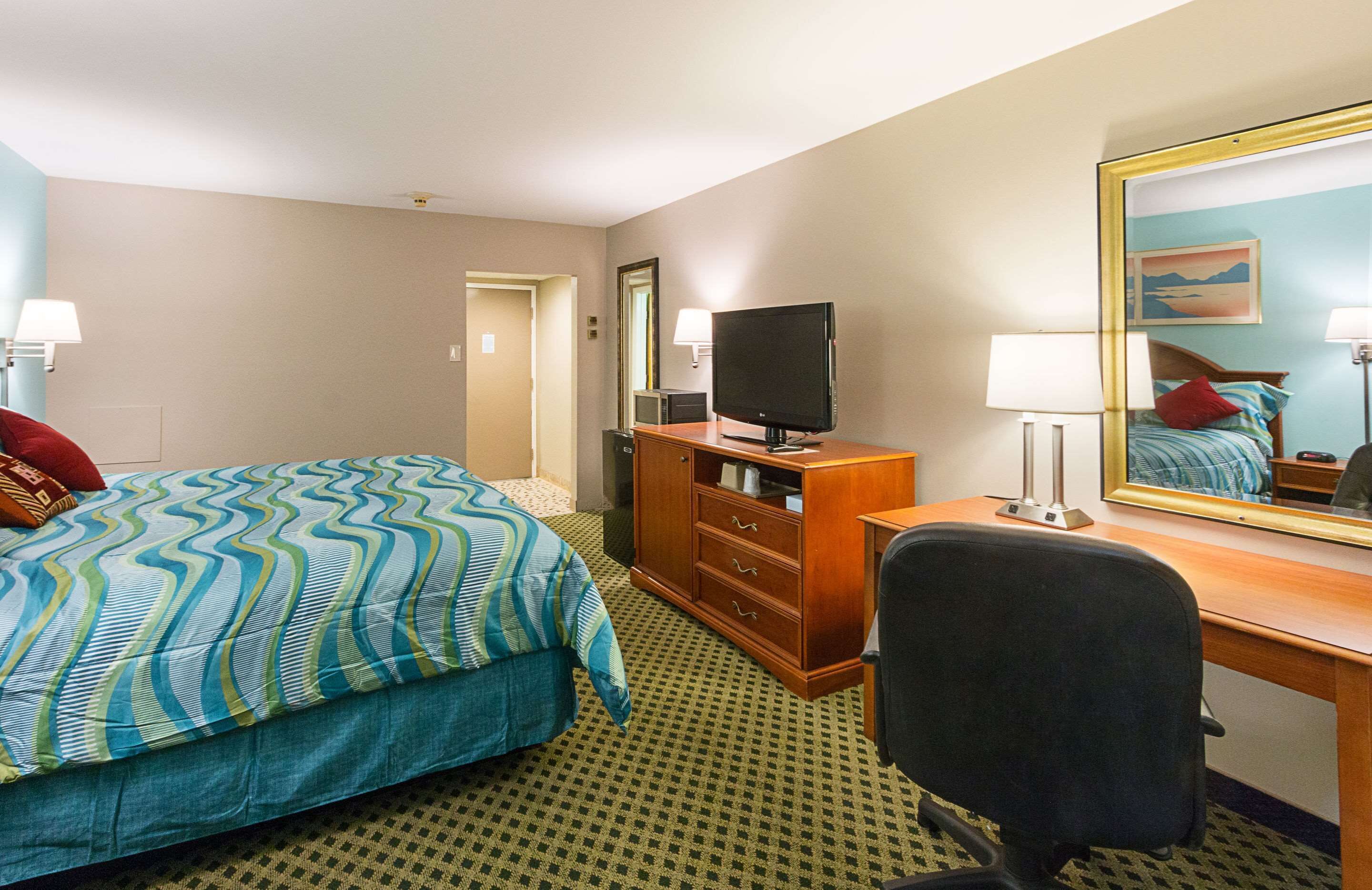 A hotel room with a bed, a desk, a chair, a television, and a mirror.