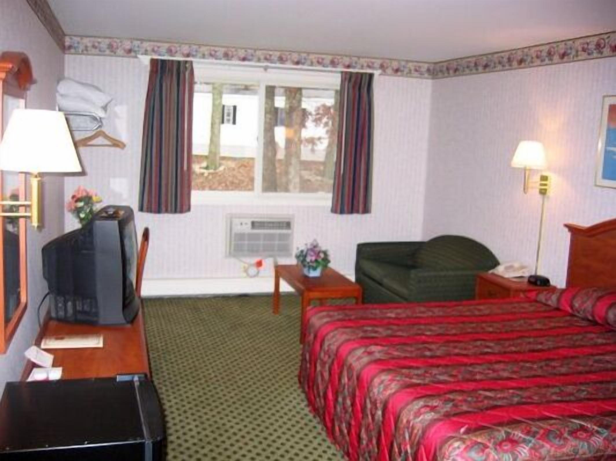 Habitación de hotel con cama, escritorio con televisor, silla y ventana con cortinas.