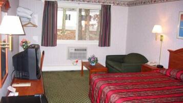 A hotel room with a bed, a desk with a television, a chair, and a window with curtains.