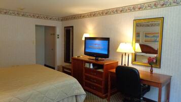Een hotelkamer met een bed, een bureau met een computer, een stoel, een lamp en een televisie waarop 'hhgregg' staat.