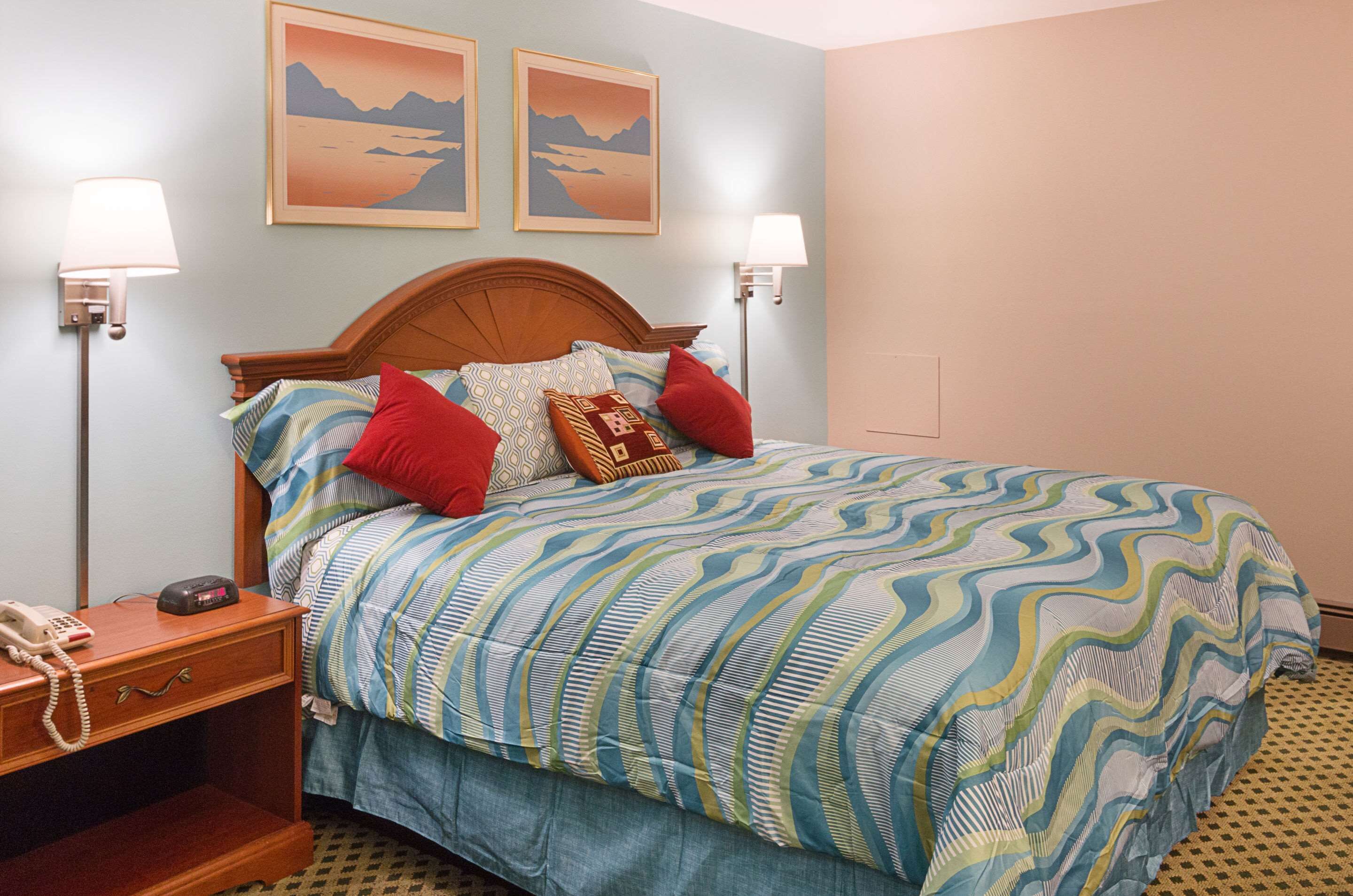 A neatly made bed with a patterned bedspread, two wall-mounted lamps, and two framed pictures on the wall.