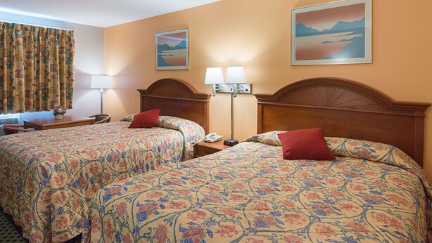 Une chambre d’hôtel avec deux lits, un bureau, une lampe et un tableau au mur.