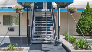 L’entrée d’un motel, avec un auvent bleu, un escalier en métal et des jardinières suspendues.