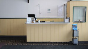 A reception desk with a computer, a phone, and a small window. There is a calendar on the wall and a sign with a phone number. -  Grapevine Inn (North East)