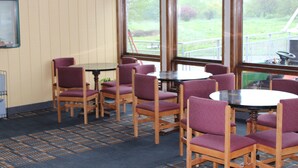 A room with wooden chairs and a round table, large windows with a view of greenery outside. -  Grapevine Inn (North East)