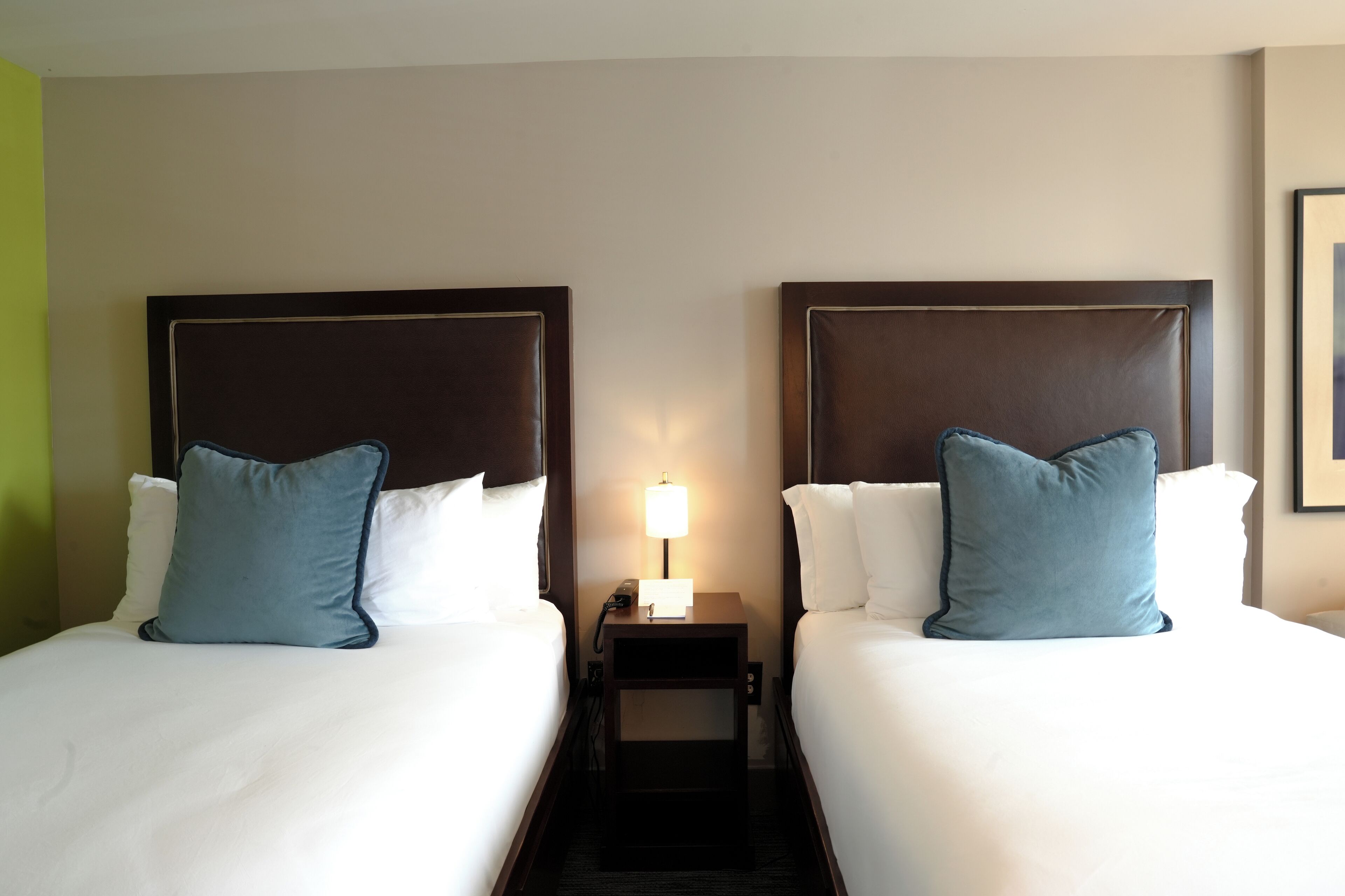 A hotel room with two beds, each with a headboard, a nightstand with a lamp, and a wall-mounted phone.