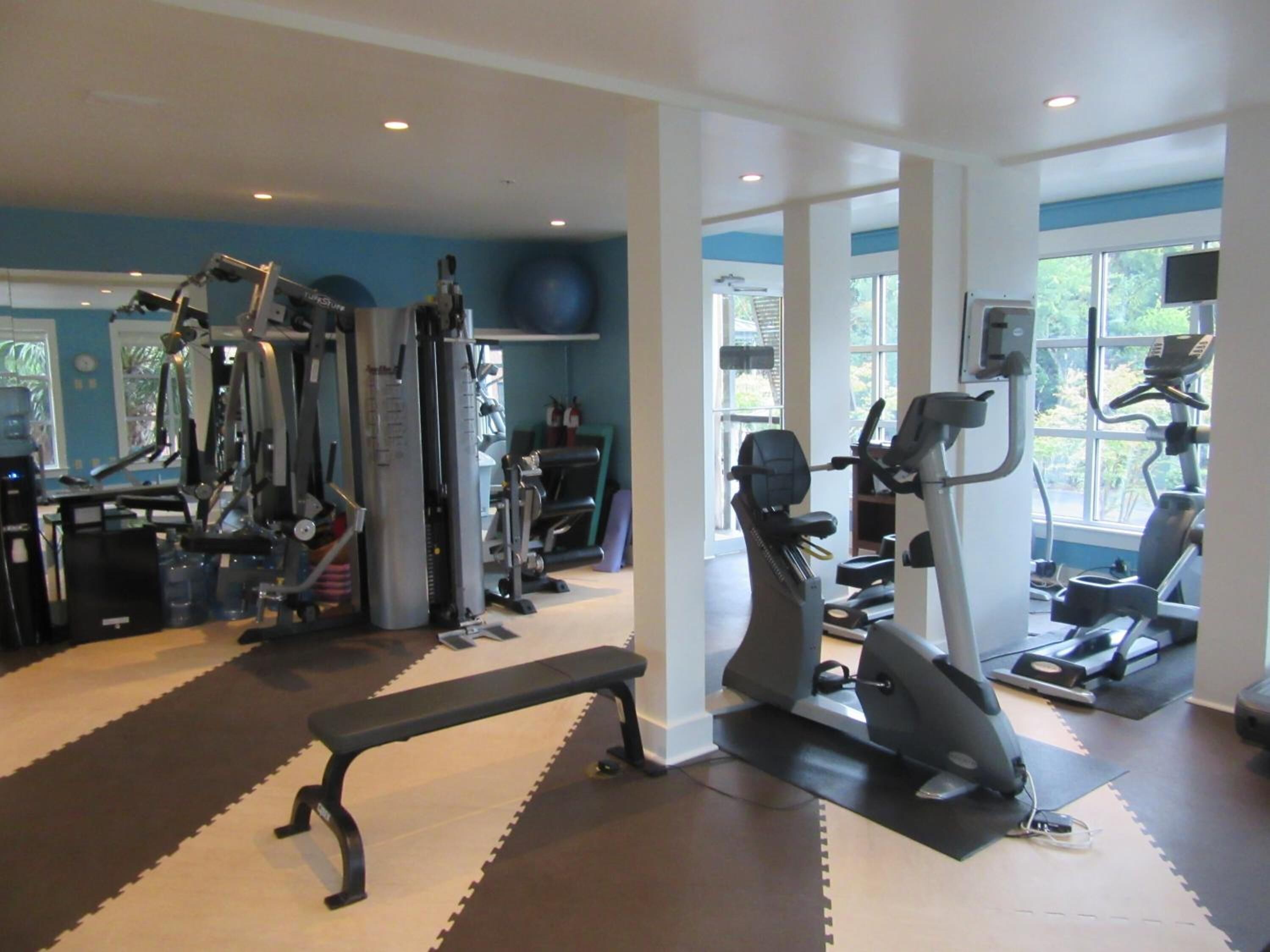 Une salle de sport équipée de divers appareils d’exercice, notamment des tapis de course et des appareils de musculation, ainsi que d’un banc.