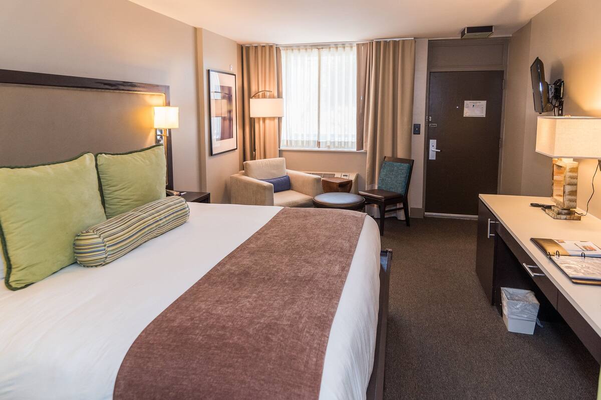 A hotel room with a large bed, a desk, a chair, and a small table.
